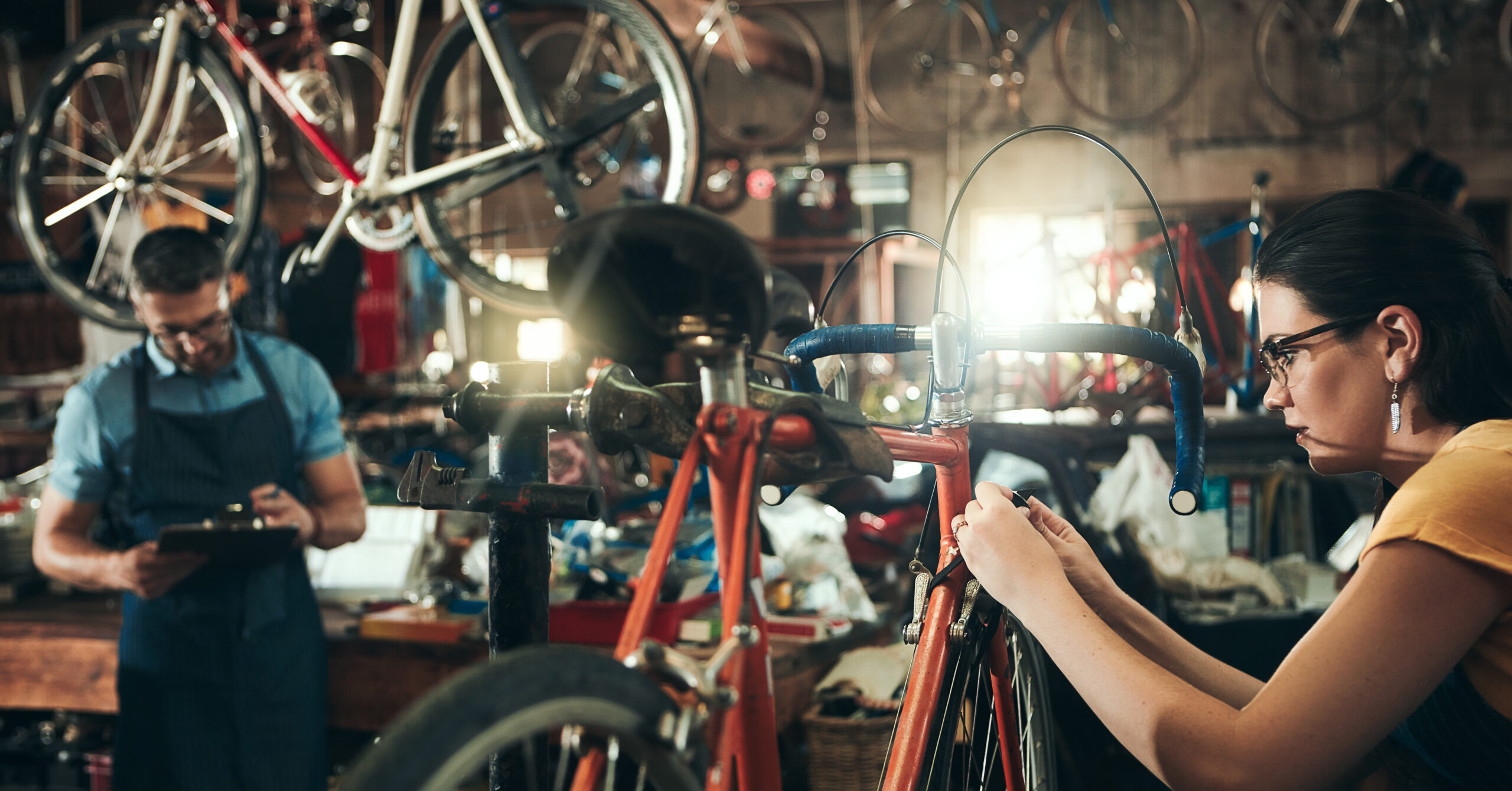 People, bicycle mechanic and fix with inspection for maintenance or small business at repair shop together. Young man, woman or cycling engineers working on bike with tools or equipment at workshop