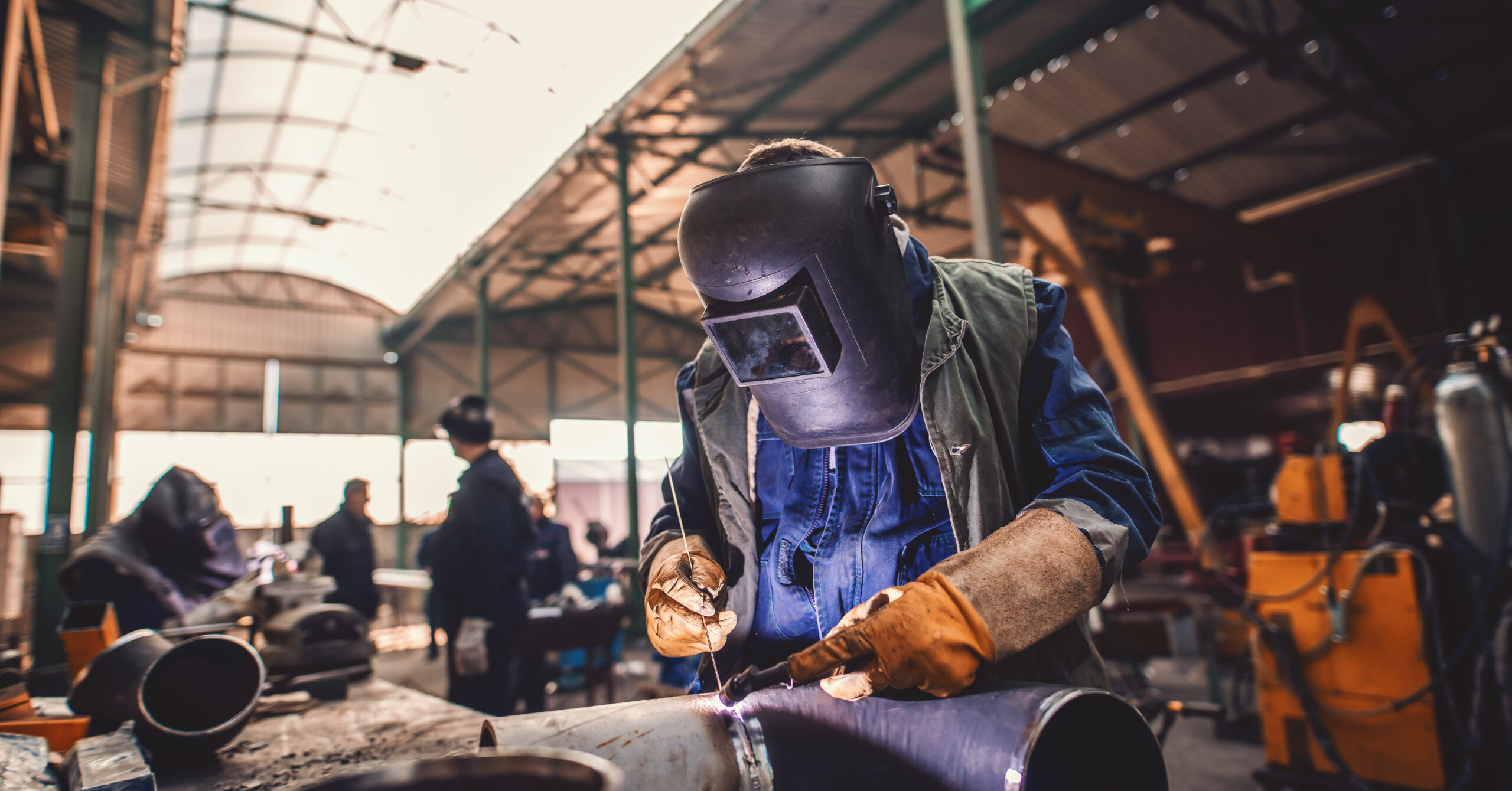 Worker welding iron. Protective suit and mask on. Workshop inter